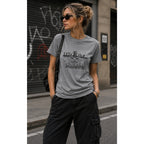 Woman wearing a gray t-shirt with text and black cargo pants on a street.